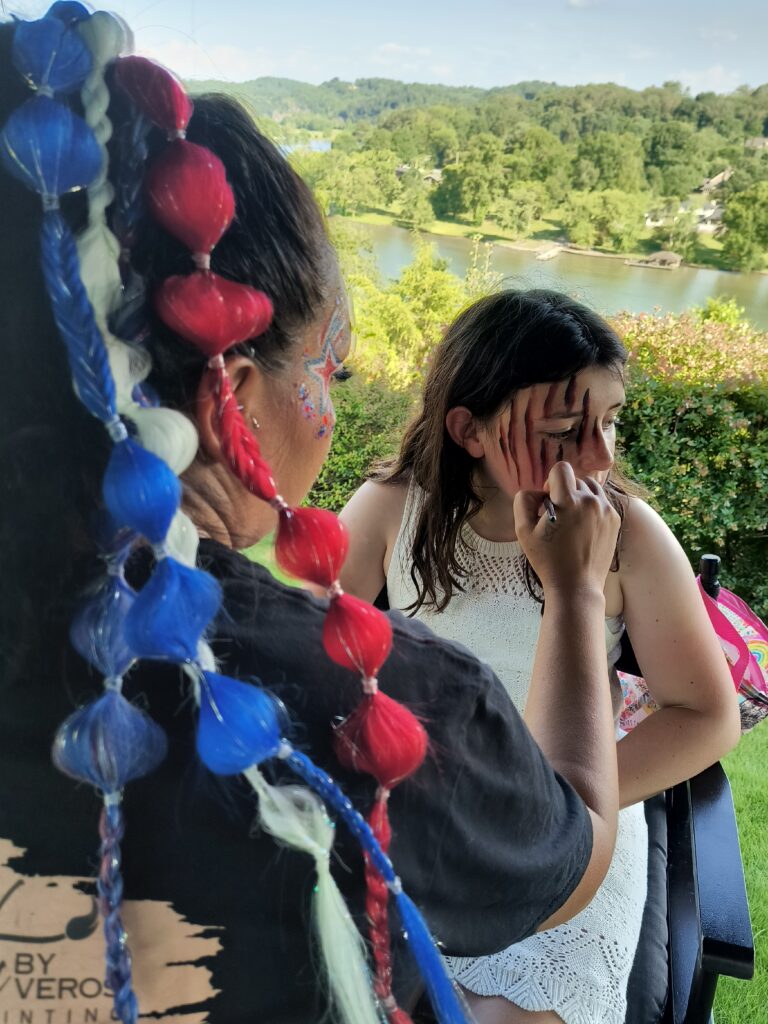 Lady with colorful braids painting a child's face