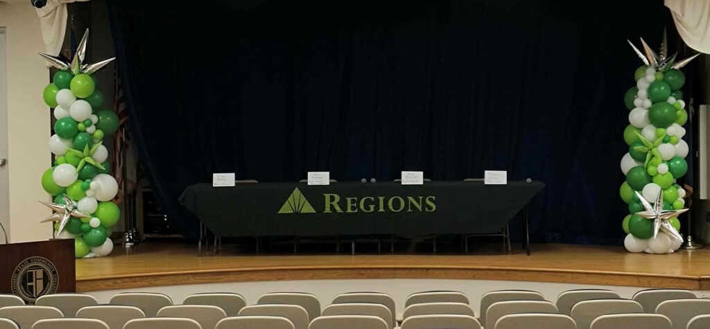 Stage with black  backdrop, tables, and green and white balloon columns on each side