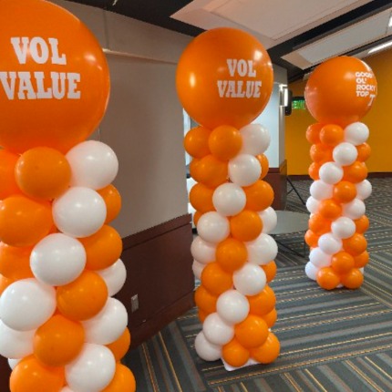 Three orange and white balloon columns with VOL VALUE branded toppers at University of Tennessee indoor event