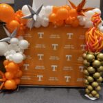 UT logo backdrop with UT torch balloon sculpture and orange and white balloon garland