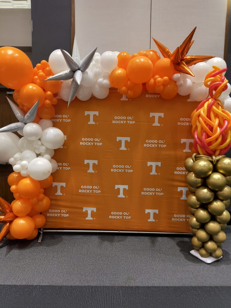 UT logo backdrop with UT torch balloon sculpture and orange and white balloon garland